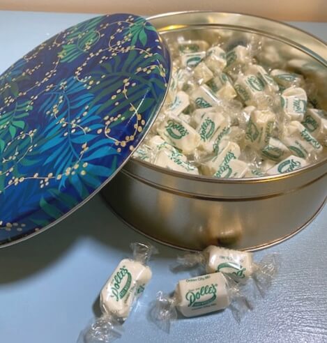 opened Holiday Mellow Mint Tin with loose taffy kisses in front